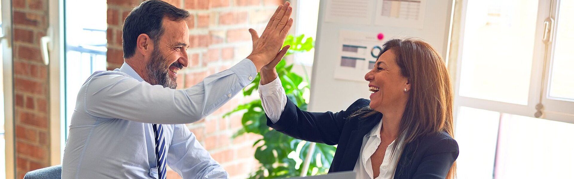 Zwei lachende Personen sitzen an einem Tisch und geben sich ein "High Five" || Foto von krakenimages auf unsplash.com