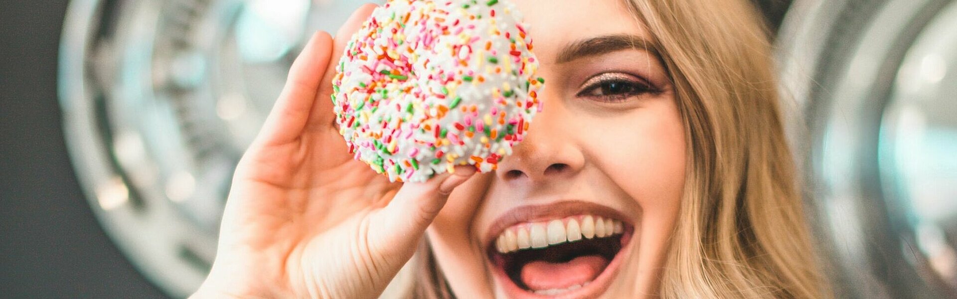Lachende junge Frau, die sich einen Donut vors Auge hält || Foto von Court Prather auf unsplash.com